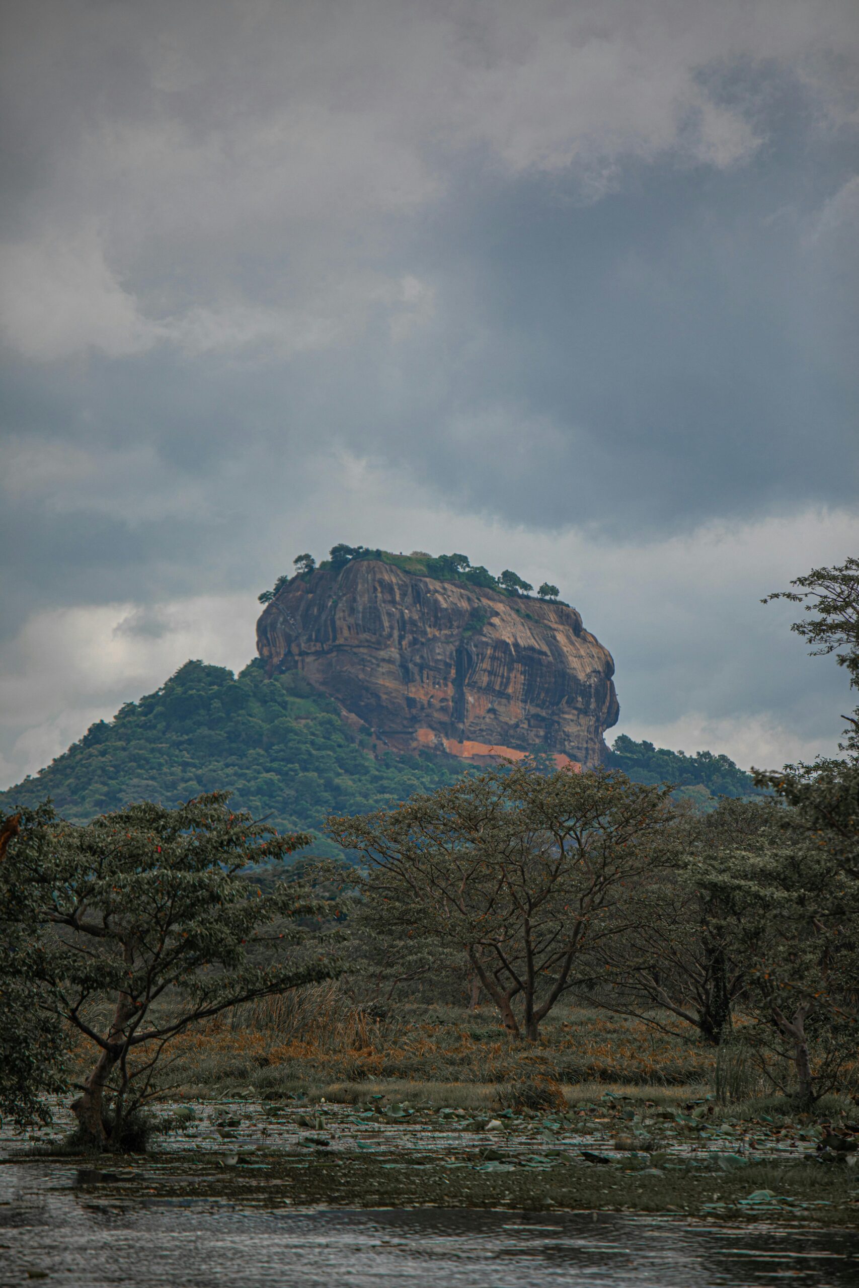 Scenic view of Sigiriya rock fortress amidst lush green nature under cloudy sky in Sri Lanka.